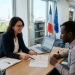Deux professionnels en bureau, document et ordinateur sur la table, discussion sur la rémunération d'un travailleur détaché, drapeaux français et européen en arrière-plan.